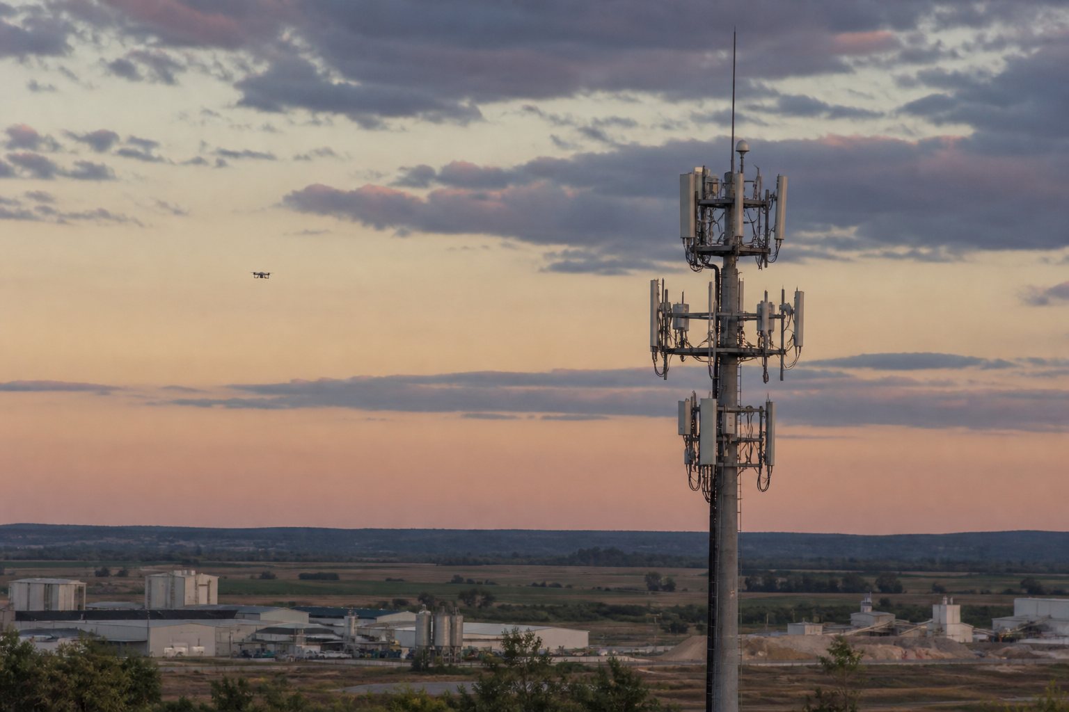 Telecommast met 5G-antennes in de schemering, met in de verte een kleine drone